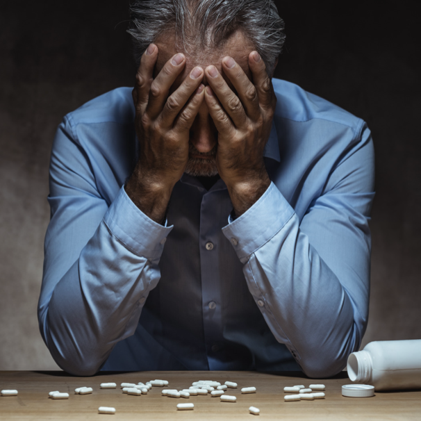 Man sitting at a table covered with pills with hands covering face
