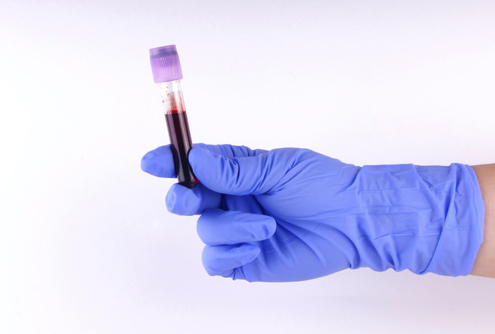 Close-up of hand holding blood sample in test tubes against white background