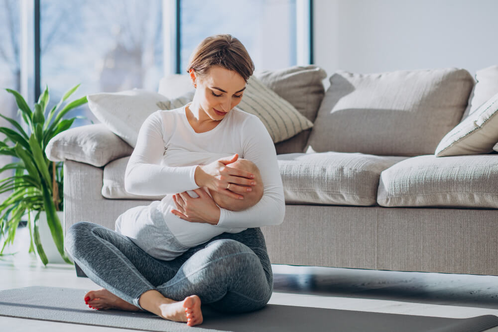 Young woman breast feeding toddler son and sitting on mat